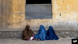 افغان خواتین امدادی ادارے سے خوراک کا راشن ملنے کے انتظار میں سڑک پر بیٹھی ہیں۔اے پی فوٹو