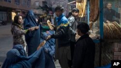 کابل کی ایک بیکری کے سامنے ایک شخص ضرورتمند خواتین میں روٹیاں تقسیم کرتے ہوئے۔ دو دسمبر، 2021ء (فائل فوٹو)